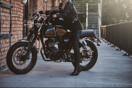 stylish female biker is sitting her black bike while posing photoshoot street